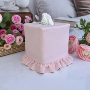 Pink linen ruffle tissue box cover front view on gray surface with wicker basket tray