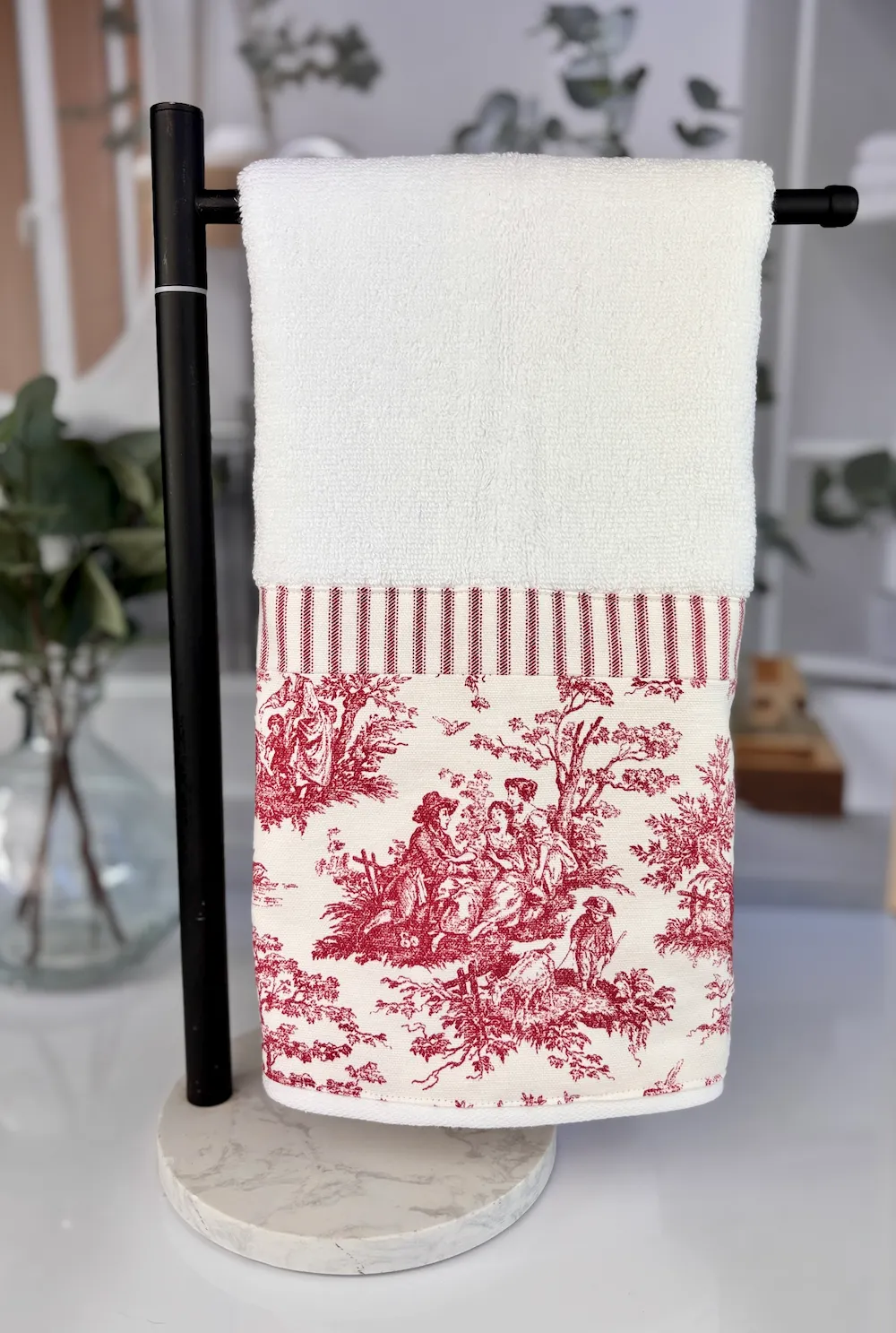 Decorative toile hand towel hanging on a black towel rack on farmhouse bathroom counter
