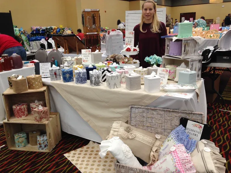Christy standing at her craft fair booth displaying handmade tissue box covers and toilet paper covers