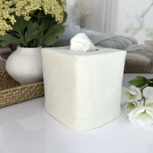 Hemstitch linen tissue box cover on bedside table with white blossoms and books