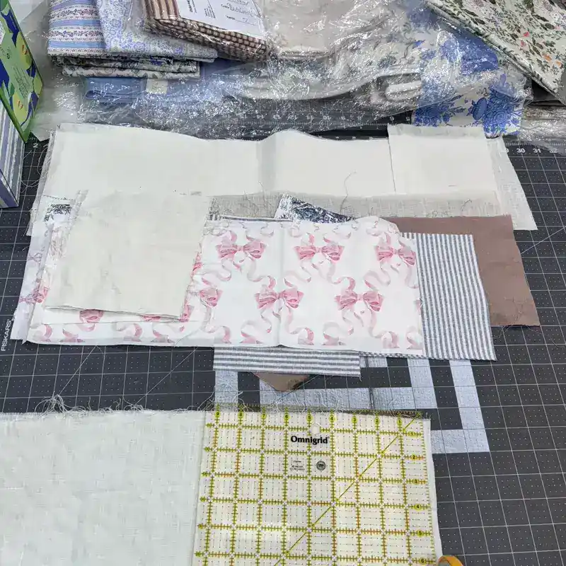 Fabric swatches including pink bow print and linen laid out on Fiskars cutting mat for tissue box cover