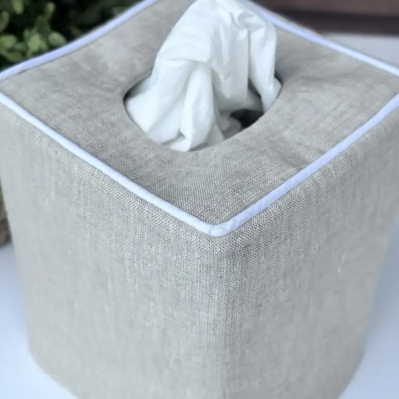 Close up of a natural linen tissue box cover with crisp white piping around the top