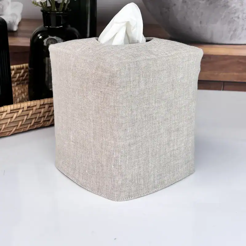 Reversible natural linen tissue box cover on a dark wood bathroom vanity with a woven basket and stone bowl