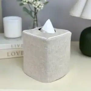 Natural linen tissue holder on a bedroom nightstand next to a white candle and stacked books, made in the USA
