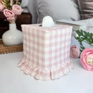 Pink gingham ruffle tissue box cover with a full ruffle skirt, shown at an angle on a nightstand