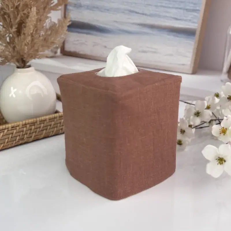 Solid brown linen tissue holder on a coastal bathroom counter with a beach print, white vase, and dried grass