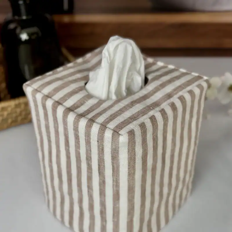 Close up of a brown and white stripe linen tissue cover on a dark wood dresser with a pleated lamp